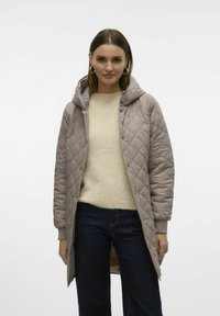 Beige gewatteerde jack met capuchon, voorzien van een drukknoopsluiting, geribbelde manchetten en een slank, middellang ontwerp. Draag het over een crèmekleurige trui en donkerblauwe jeans.