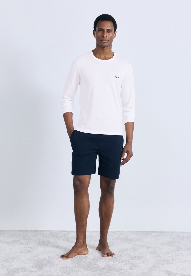 Light pink long-sleeve shirt with "BOSS" logo, paired with dark navy shorts. The fabric appears smooth, and the fit is casual, with side pockets.