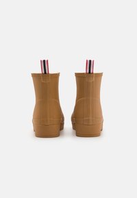 Gummistiefel in Braun mit glatter Oberfläche, ausgestattet mit einer gestreiften Zuglasche in Rot, Schwarz und Weiß. Runde Zehenform und strukturierte Sohle.