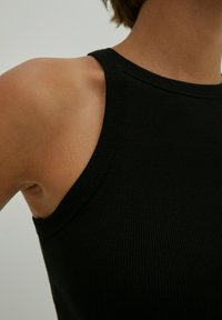 Schwarzes geripptes Tanktop mit rundem Ausschnitt und breiten Trägern. Der Stoff wirkt weich und hat eine figurnahe Passform.