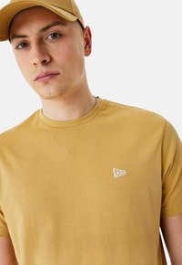 T-shirt en coton jaune avec un col rond, arborant un petit logo blanc sur la poitrine gauche. Texture lisse et coupe standard.