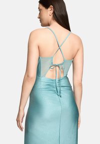 Robe de soirée turquoise à silhouette ajustée, avec un panneau arrière transparent, des bretelles croisées et des détails froncés à la taille.