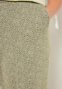 Tkané kalhoty v zeleno-krémovém herringbone vzoru, s bočními kapsami a měkkou, strukturovanou tkaninou. Přiléhající pas, volnočasový design.