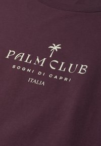 Dark purple fabric with white text "PALM CLUB" and small palm tree icon above, followed by "SOGNI DI CAPRI" and "ITALIA" below.