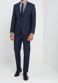 Tmavě modrý oblek s upraveným střihem, sako na jeden knoflík, klopami s výřezem a odpovídajícími kalhotami; doplněný kostkovanou košilí na knoflíky a kravatou.