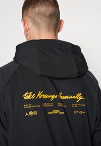 Sweat à capuche noir avec cordon de serrage, arborant un texte jaune indiquant "Take Mornings Personally" et "Jordan Breakfast Club" avec un logo.