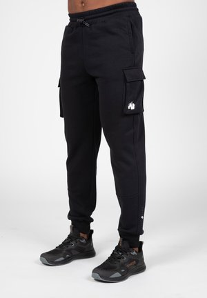 Schwarze Cargo-Jogger aus weichem Stoff, mit Seitentaschen, elastischem Bund und gerippten Bündchen. Mit Logodetail am Oberschenkel.