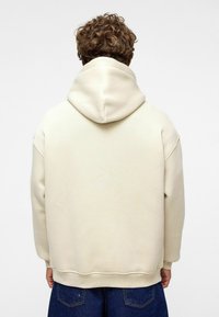 Crème-kleurige hoodie met een grote, ronde capuchon. Gemaakt van gladde stof, heeft verlaagde schouders en een comfortabele pasvorm. Eenvoudig ontwerp.