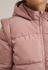Rožinė pūkinė striukė su kapišonu, turinti zip užsegimą, minkštą vidinį pamušalą ir siuvinėtą dizainą. Audinys yra sklandus, blizgus.