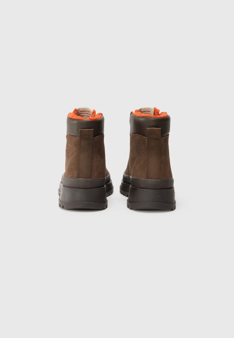 Braune Knöchelstiefel aus Wildleder, graue Gummisohlen, elastische Seitenpanels und ein leuchtend oranger Fleece-Futter.