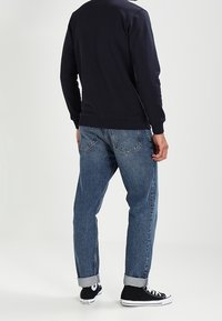 Sudadera navy de mangas largas, combinada con unos vaqueros de denim azul claro. Los vaqueros tienen los puños enrollados y bolsillos traseros con acentos de costura. Zapatillas negras.