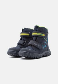 Mørkeblå barnestøvler med kontrasterende grønne og blå detaljer, utstyrt med borrelåsremmer, en robust gummisåle og forsterket tåparti.