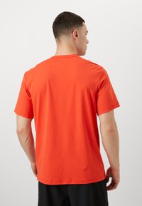 Lühikeste varrukatega, ümmarguse kaelusega t-särk erksas oranžis puuvillas, millel on sile tekstuur ja lõdva lõige. Minimalistlik detail tagaküljel.