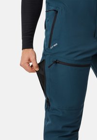 Blauwe waterdichte outdoorbroeken met ritszakken, ventilatieroosters en een slim fit. Kenmerkt zich door contrasterende zwarte accenten en een gestructureerde stof.