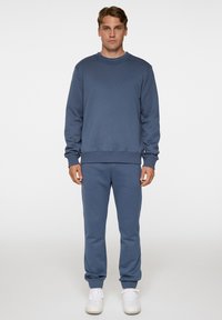 Sininen puuvillaneule, jossa on pitkät hihat ja pyöreä pääntie, yhdistettynä samansävyisiin housuihin. Molemmissa on rento istuvuus ja ribbireunat.