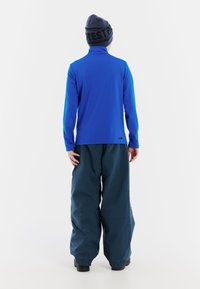 Top blu lungo a maniche con colletto alto e cuciture piatte abbinato a pantaloni larghi blu scuro. Entrambi realizzati in materiali leggeri e funzionali.