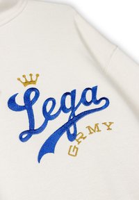 Kremowa bluza z niebieskim i złotym haftowanym napisem "Lega GRMY" z złotą koroną nad literą "L". Miękka tekstura, casualowy design.