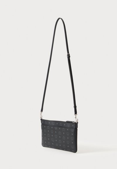 Sac bandoulière noir avec bandoulière réglable et motif discret de logo sur l'ensemble, présenté suspendu sur un fond clair.