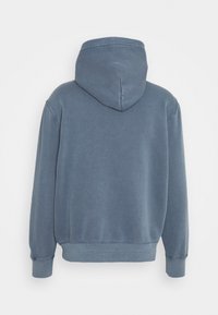 Sininen huppari, näkyy takaa, pitkähihaisena ja ribatulla hihansuulla ja helman kanssa, esillä yksinkertaisen valkoisen taustan edessä.