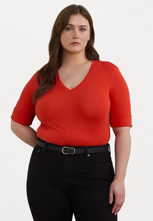 Röd kortärmad V-ringad topp med en figurnära design. Kombinerad med högmidjade svarta jeans och ett svart bälte med en silvrig spänne.