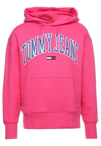 Sudadera rosa con "TOMMY JEANS" bordado en blanco y azul, con un pequeño logotipo como acento. Incluye un bolsillo frontal y capucha con cordón.
