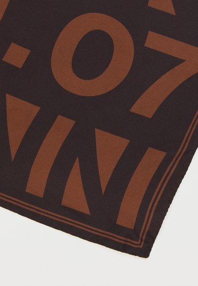 Σκούρο ύφασμα με μεγάλα καφέ γεωμετρικά σχήματα και αριθμούς, με ραμμένο τελείωμα και διπλή γραμμή περιγράμματος σε μια γωνία.