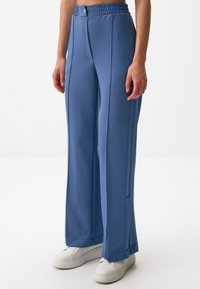 Jasnoniebieskie szerokie spodnie wykonane z miękkiego materiału, z wysokim elastycznym paskiem w talii i detalami na szwach bocznych. W połączeniu z białymi trampkami.