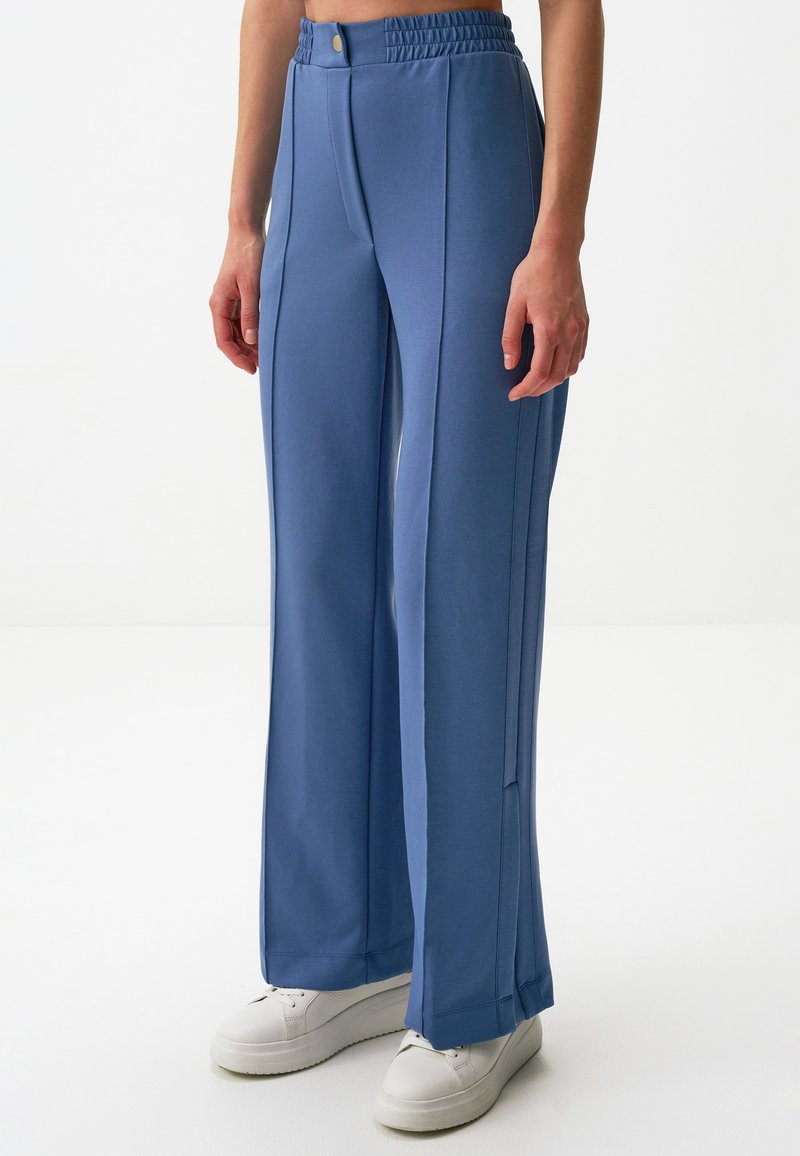 Jasnoniebieskie szerokie spodnie wykonane z miękkiego materiału, z wysokim elastycznym paskiem w talii i detalami na szwach bocznych. W połączeniu z białymi trampkami.