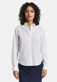 Weißes Baumwollhemd mit Knopfleiste, das einen klassischen Kragen, lange Ärmel und einen leicht abgerundeten Saum aufweist. Einfaches Design, ohne Muster.
