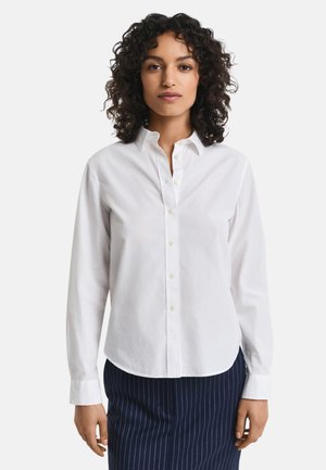 Hvit skjorte med knapper laget av bomull, som har klassisk krage, lange ermer og en lett buet søm. Enkel design, uten mønstre.