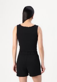Top negro corto con escote en forma de ondas, combinado con pantalones cortos negros. La tela parece suave y ajustada al cuerpo. Diseñado sin estampados.