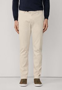 Beżowe bawełniane spodnie o prostym kroju, z przednimi kieszeniami i pojedynczym zapięciem na guzik. Noszone z brązowymi sneakersami.