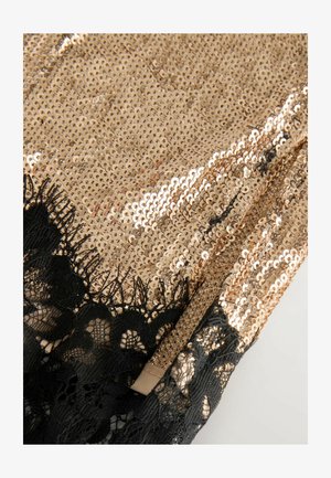 Goldener Paillettenstoff mit schwarzem Spitzenrand, der eine glatte Textur und einen schimmernden Glanz aufweist, an einer Kante gefaltet, wobei die Spitzenverzierung sichtbar ist.