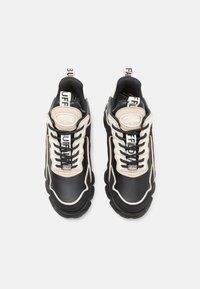 Schwarze und cremefarbene Sportschuhe mit einer kräftigen Sohle, strukturiertem Leder, auffälligen Schnürsenkeln und Logo-Details auf der Zunge und der Ferse.