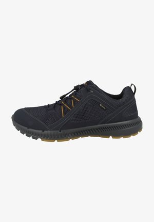 Zapatilla atlética de malla negra con suela de goma gris, acentos naranjas en contraste y etiqueta impermeable Gore-Tex. Presenta cordones elásticos para ajuste.