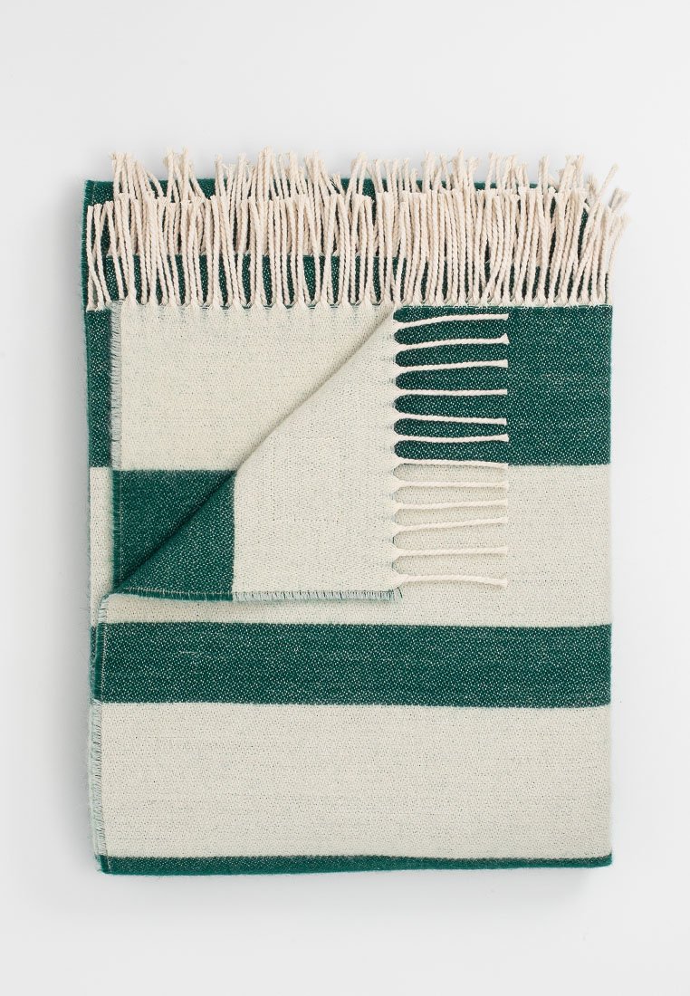 Gewebte Decke mit abwechselnden grünen und cremefarbenen Streifen, mit ausgefransten Kanten und einer weichen Textur. Rechteckige Form, ordentlich gefaltet.