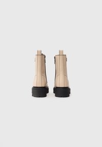 Bottines en cuir beige avec des semelles épaisses noires, des zips arrière visibles et des coutures épaisses sur fond blanc uni.
