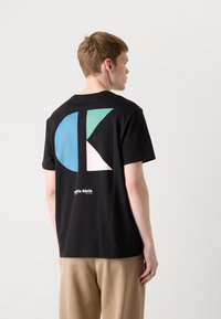 Sort bomulds t-shirt med et stort abstrakt design i teal, pink og hvid på ryggen. Indeholder "calvin klein" logoet nederst.