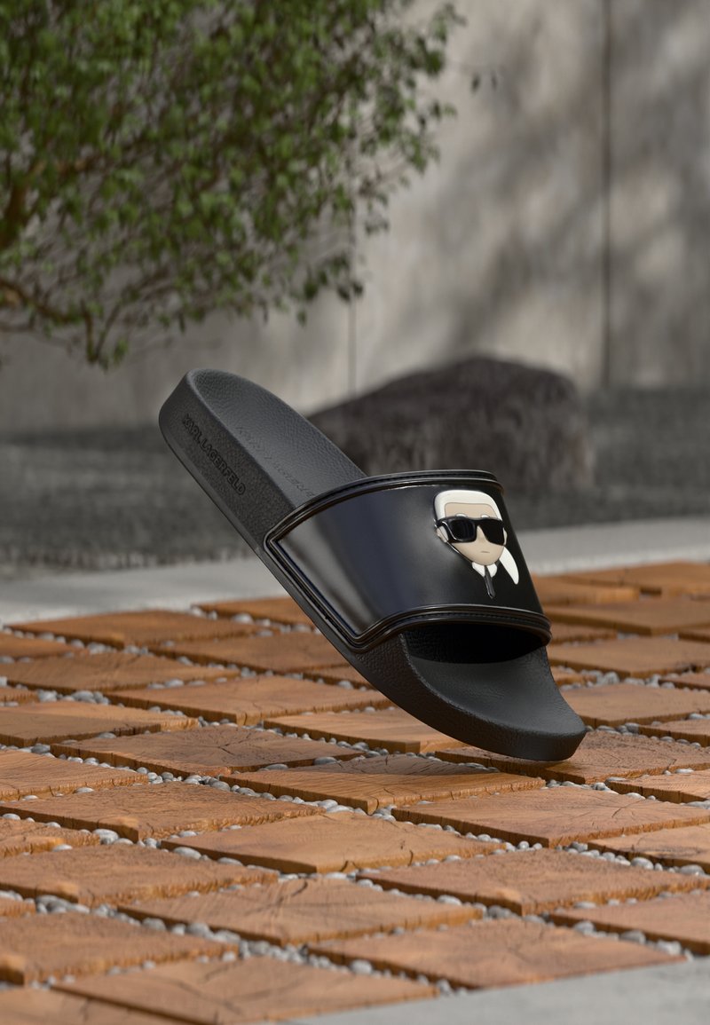 Μαύρο σανδάλι με φάσα, με καρτούν φιγούρα που φοράει γυαλιά ηλίου στη φάσα, εκτεθειμένο έξω πάνω σε ξύλινες πλακάκια με φόντο πράσινα φυτά.