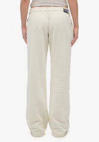 Crème-kleurige sweatpants met een relaxte pasvorm, elastische tailleband en een klein label aan de achterkant. Zacht materiaal met een gladde textuur.