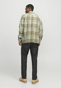 Geruite blouse in gedempte groene en beige tinten, ruime pasvorm met lange mouwen, gecombineerd met donkere denim jeans en beige schoeisel.