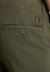 Pantaloni cargo in tessuto verde oliva con tasca posteriore, dotati di una piccola etichetta Timberland e chiusura a bottone circolare.