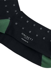 Sorte sokker med et subtilt gråt H-mønster, grønne detaljer ved skaftet og et mærke, der siger "HACKETT LONDON, HAND LINKED TOE."