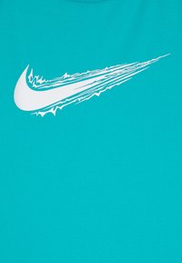 T-shirt de sport turquoise en tissu doux, arborant un grand logo Nike en blanc avec des accents dynamiques et marqués sur le côté gauche.