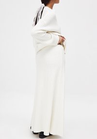 Maglione bianco a coste abbinato a una lunga gonna coordinata. Presenta una vestibilità rilassata, un tessuto texturizzato e calzature nere.