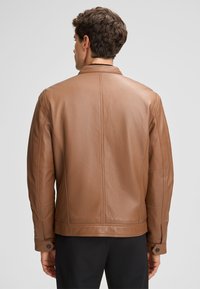 Bruine leren jas met een gladde textuur, voorzien van een hoge kraag, gestikte accenten en knopen met drukknoopsluiting bij de mouwen. Achteraanzicht weergegeven.