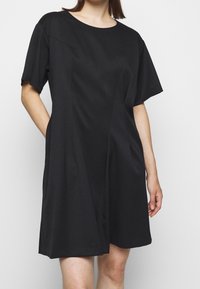 Svart kortärmad klänning med rund halsringning, med en skräddarsydd passform, sidofickor och subtila sömdetaljer för en strukturerad silhuett.