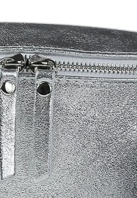 Zilveren metallic zak met een gestructureerd oppervlak, voorzien van een ritssluiting en glanzende hardware details.