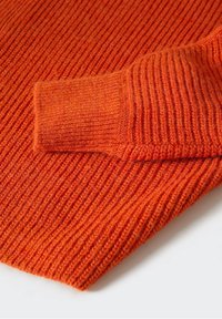 Manche de pull en maille côtelée orange repliée sur un fond en tissu côtelé orange, mettant en valeur la texture et le motif de la maille.