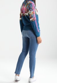 Blue patterned sweatshirt with pink side stripes, paired with light blue fitted jeans and white sneakers. Back view displays design details.